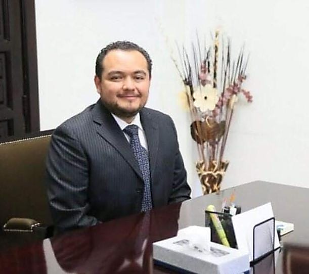 Un hombre con un traje de color negro sobre una mesa Descripción generada automáticamente con confianza media